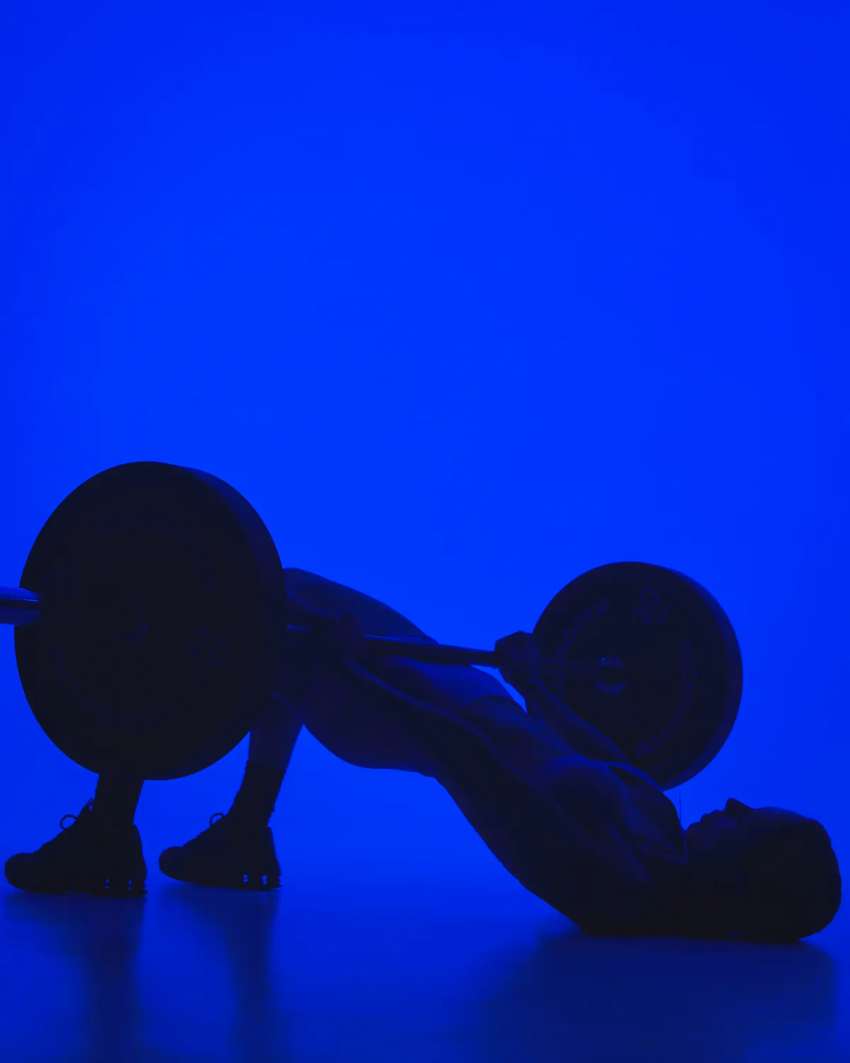 Jules in silhouette driving a loaded barbell through a hip thrust